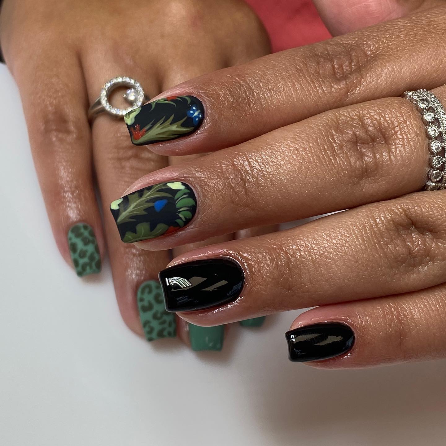 Hand-painted black nails with green foliage, colorful accents, and leopard print nail art by Rita